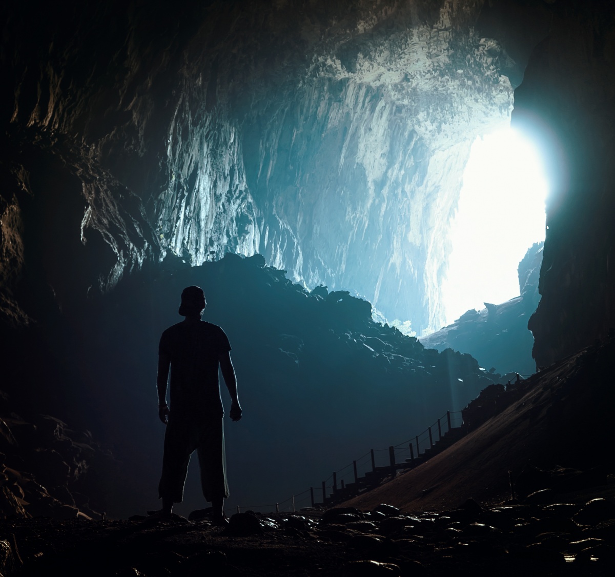 Picture of very large cave and light flowing inside. A man standing in cave looking at the entrance.