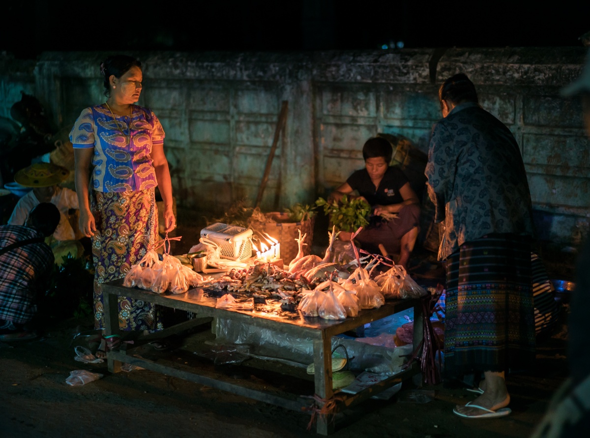 Photo of candle light marketplace table full of chicken. There are three women around the table.