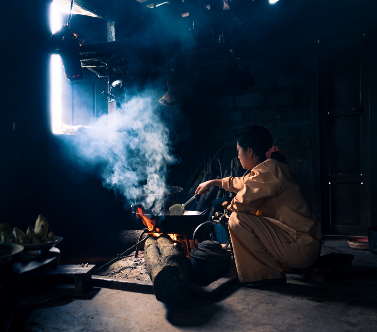 Photo of Traditional Palaung Kitchen in Kalaw, Myanmar. The kitchen is filled with smoke and a girl is cooking by open fire stove.